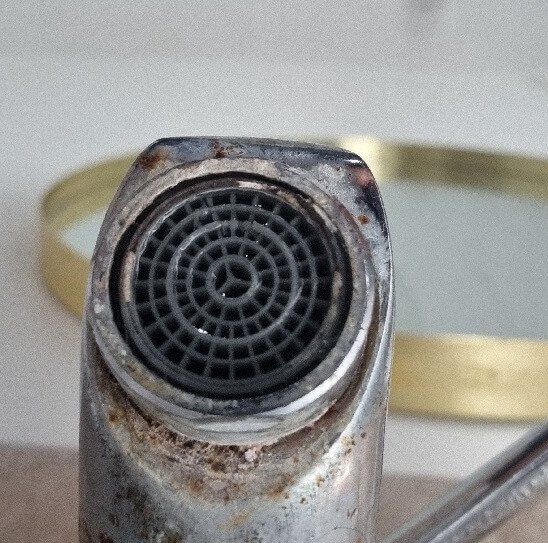 Close-up of a heavily scaled tap aerator with visible corrosion, demonstrating increased Legionella risk in a domestic childcare environment